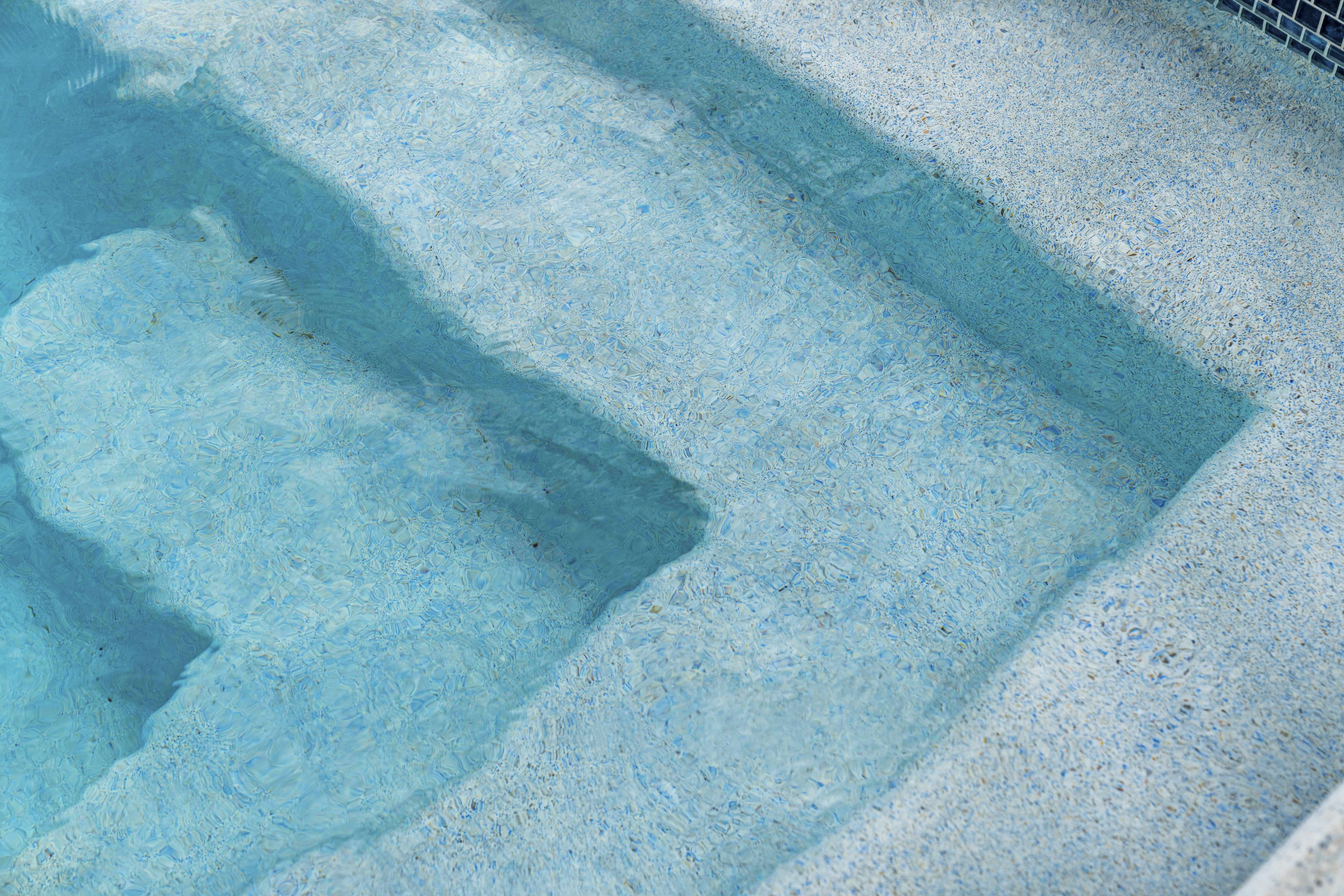 Pebble finish pool interior in sunlight, aggregate texture with warm lagoon-like water color